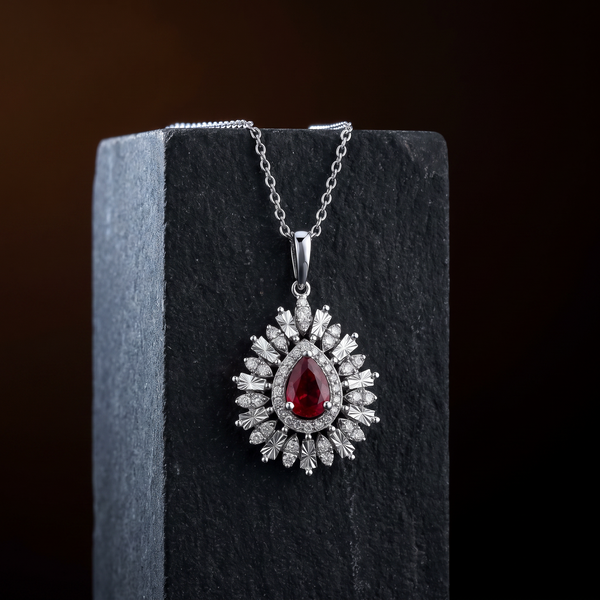 The Lantern Necklace draped over dark basalt stone, a pear cut ruby in a diamond halo inside engraved rays