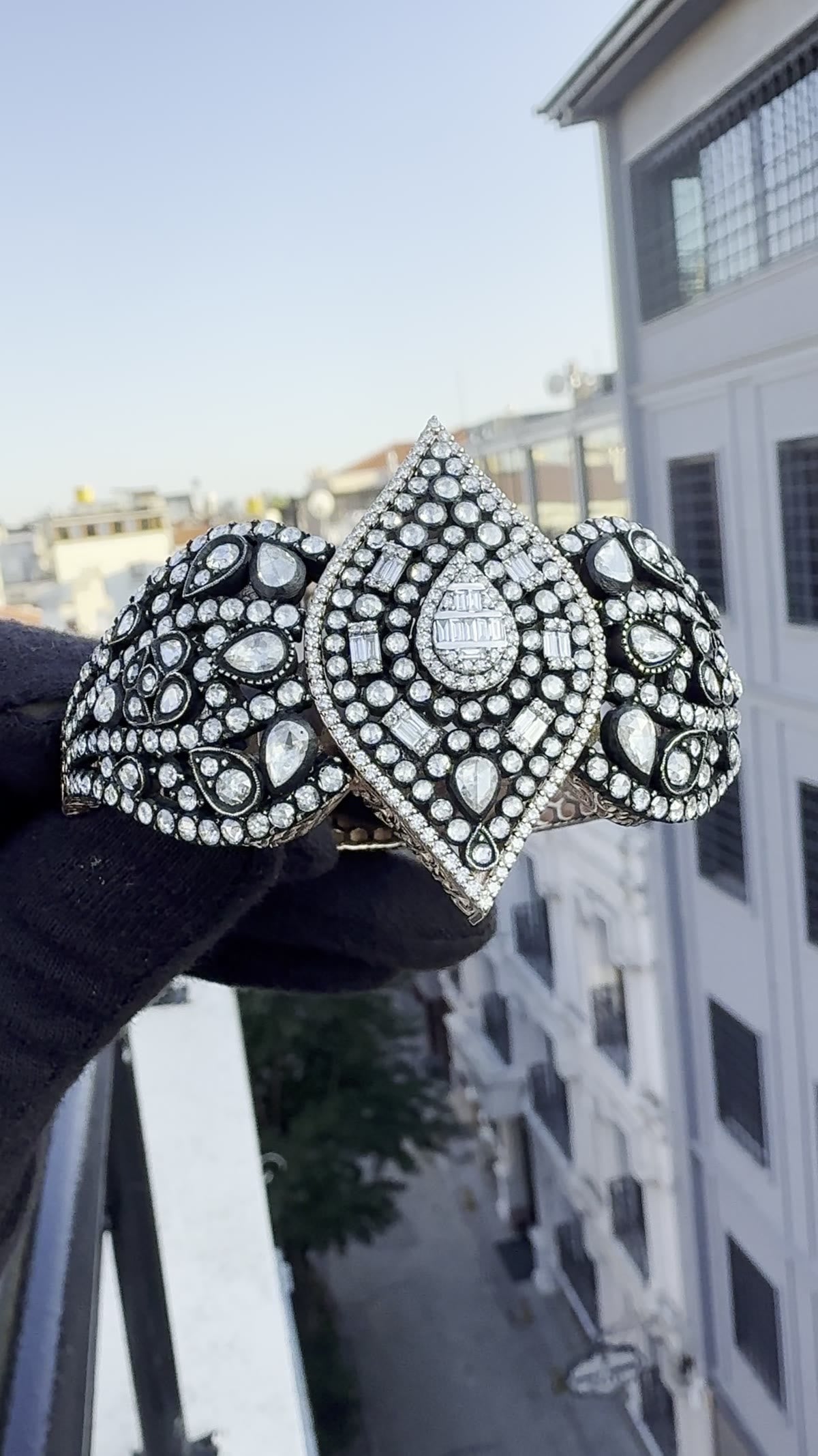 Blackened cuff set with rose-cut diamonds, held over the rooftops
